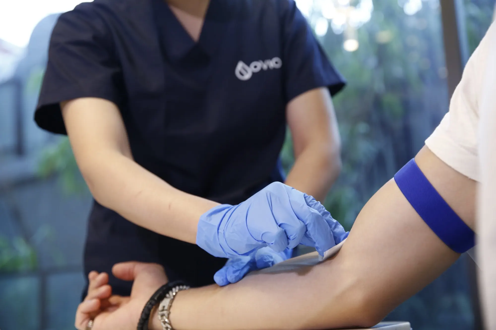 An Ovio nurse in gloves preparing a client's arm for a blood draw, with a tourniquet on his upper arm